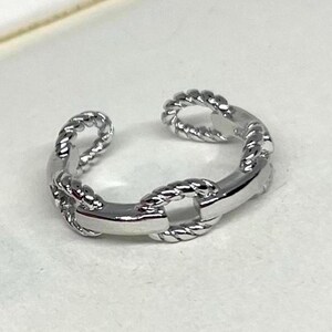 May include: A silver-colored adjustable ring with a chain link design. The ring features a combination of smooth and twisted rope-like textures, creating a unique and stylish accessory. The open design allows for an adjustable fit.