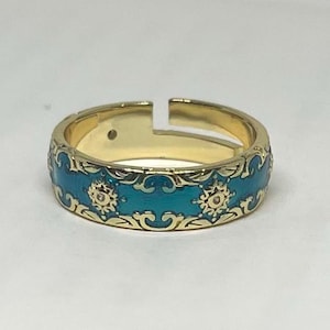 Peut inclure: Une bague dorée avec une bande en émail turquoise. La bande présente des filigranes dorés ornés et deux motifs circulaires. La bague a un design ouvert et une petite pierre précieuse. Bijoux.