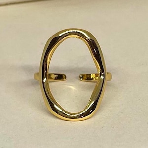 May include: A gold-colored ring with an open oval design. The ring has a smooth, polished finish and a split band. The oval shape is slightly irregular, adding a unique touch to the jewelry.