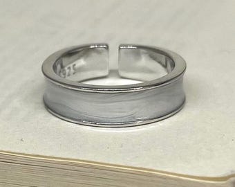 May include: A silver-colored adjustable ring with a wide band. The ring has a smooth, polished finish with a lighter, textured enamel-like center. The inside of the ring is stamped with "925".