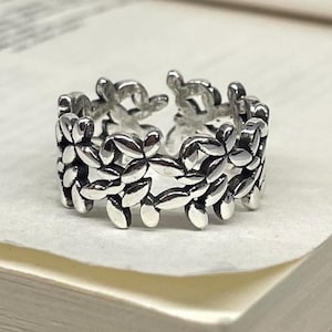 May include: A silver ring with a repeating leaf pattern. The ring has an open design, allowing for size adjustments. The leaves are detailed, creating a textured look. A stylish piece of jewellery for everyday wear.