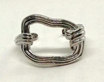 May include: A silver-toned cuff bracelet with a unique, knotted design. The bracelet features a rectangular shape with rounded corners, and the metal appears to be intricately woven. The design is modern and eye-catching.
