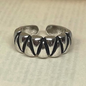 Puede incluir: Un anillo plateado con un diseño único. El anillo presenta una serie de segmentos redondeados y acanalados, creando una apariencia texturizada. El diseño abierto permite un ajuste de tamaño. El anillo es probablemente de metal.