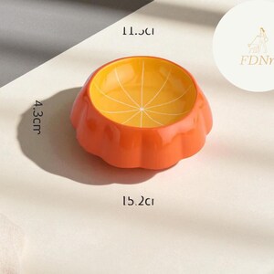 May include: Orange ceramic pet bowl with a citrus fruit design. The bowl is 15.2 cm wide, 11.5 cm long, and 4.3 cm high. The interior is yellow with a segmented pattern, and the exterior is orange.