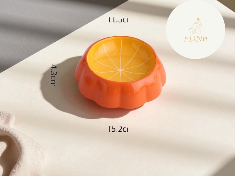 May include: Orange ceramic pet bowl with a citrus fruit design. The bowl is 15.2 cm wide, 11.5 cm long, and 4.3 cm high. The interior is yellow with a segmented pattern, and the exterior is orange.