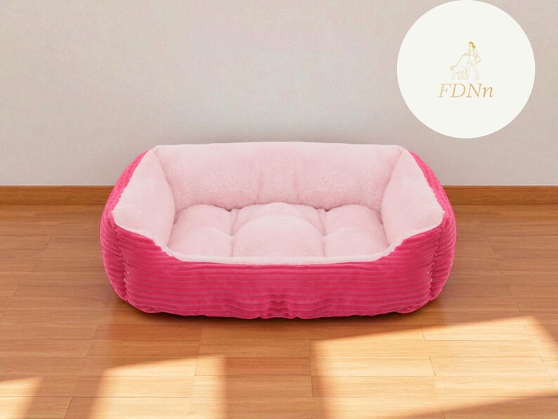 K&ouml;nnte beinhalten: Ein pinkfarbenes Haustierbett mit einem weichen, hellrosa Innenraum und einem Cord-Au&szlig;enmaterial. Das Bett hat eine rechteckige Form mit erh&ouml;hten Seiten und einer gepolsterten Mitte. F&uuml;r kleine Haustiere.
