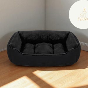 K&ouml;nnte beinhalten: Ein schwarzes Haustierbett mit einem pl&uuml;schigen, dunkelgrauen Innenraum. Das Bett hat eine rechteckige Form mit erh&ouml;hten Seiten und einer gepolsterten Mitte. Das Bett steht auf einem Holzboden, mit einem Logo im Hintergrund.