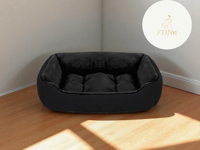 K&ouml;nnte beinhalten: Ein schwarzes Haustierbett mit einem pl&uuml;schigen, dunkelgrauen Innenraum. Das Bett hat eine rechteckige Form mit erh&ouml;hten Seiten und einer gepolsterten Mitte. Das Bett steht auf einem Holzboden, mit einem Logo im Hintergrund.