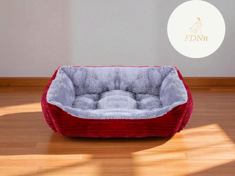 K&ouml;nnte beinhalten: Ein rechteckiges Haustierbett mit einem weichen, grauen Innenraum und einem tiefroten, cordartigen Au&szlig;enmaterial. Das Bett hat einen erh&ouml;hten Rand und ist auf Komfort ausgelegt. Das Bett steht auf einem Holzboden.