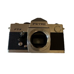 May include: A vintage Petri FTX camera with a silver and black body. The camera has a prominent lens and the word "PETRI" is printed on the top. The model name "FTX" is visible on the side. A classic film camera.