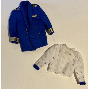 May include: A blue pilot's jacket with gold stripes and accents, and a white long-sleeve shirt with a pattern of gold airplanes. The jacket has gold stripes on the sleeves and a gold emblem.