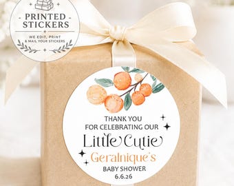 May include: A square brown gift box tied with a cream ribbon, featuring a round white sticker with a watercolor orange branch illustration and the text: THANK YOU FOR CELEBRATING OUR Little Cutie Geralnique's BABY SHOWER 6.6.26 with star icons.