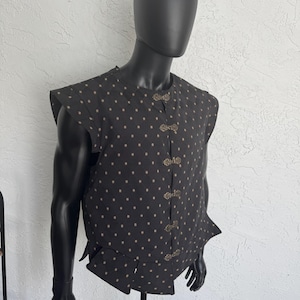 May include: A sleeveless black vest featuring a quilted diamond pattern with small gold-colored floral accents. The garment has a round neckline and is secured down the front with five ornate, metallic, decorative toggle-style fasteners.