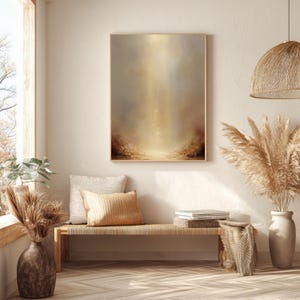 May include: A framed abstract painting with a warm color palette of beige, gold, and brown. The artwork features a central light source, creating a sense of depth and ethereal beauty. The painting is displayed in a well-lit, neutral-toned room.