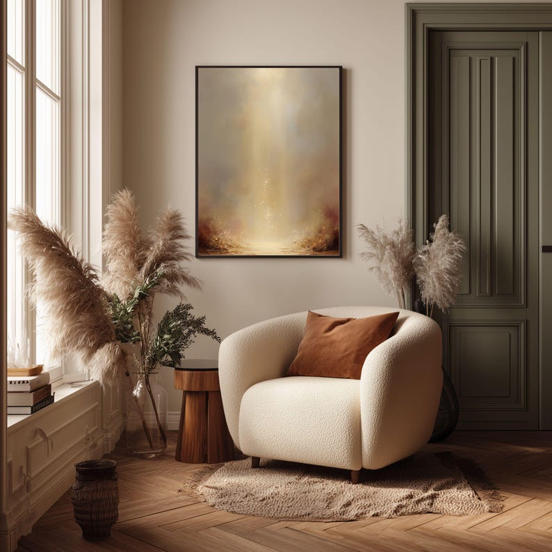 May include: A cozy living room scene featuring a cream-colored armchair with a brown throw pillow. A framed abstract painting hangs on the wall. The room is decorated with pampas grass and a wooden side table, creating a warm and inviting atmosphere.