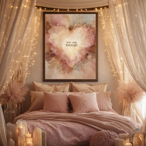 May include: A bedroom scene with a large framed artwork featuring a heart-shaped design in shades of pink, peach, and gold. The artwork has the text "YOU ARE Enough". The bed is covered in pink bedding with matching pillows. Fairy lights and candles add to the ambiance.