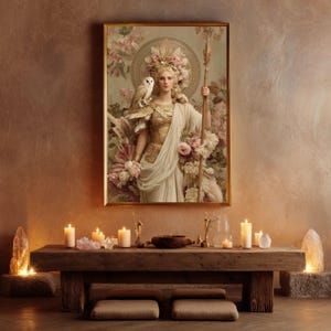 May include: A framed artwork depicts a woman in classical attire, holding a spear and adorned with an owl. The painting features a gold frame and is surrounded by floral elements. The scene is set in a room with candles and a wooden table.