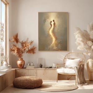 May include: A framed rectangular wall art piece featuring an abstract painting of two ethereal figures connected by a glowing golden light against a soft beige and brown background, displayed in a neutral-toned room with natural lighting.