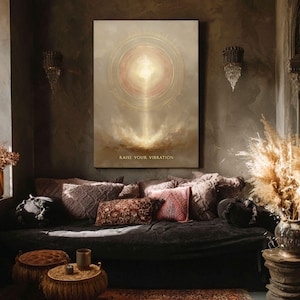 Pode incluir: Uma grande obra de arte em tela retangular com um design circular dourado e o texto "RAISE YOUR VIBRATION" em ouro. A obra de arte está pendurada acima de um sofá escuro com almofadas decorativas. O quarto tem uma estética boêmia.