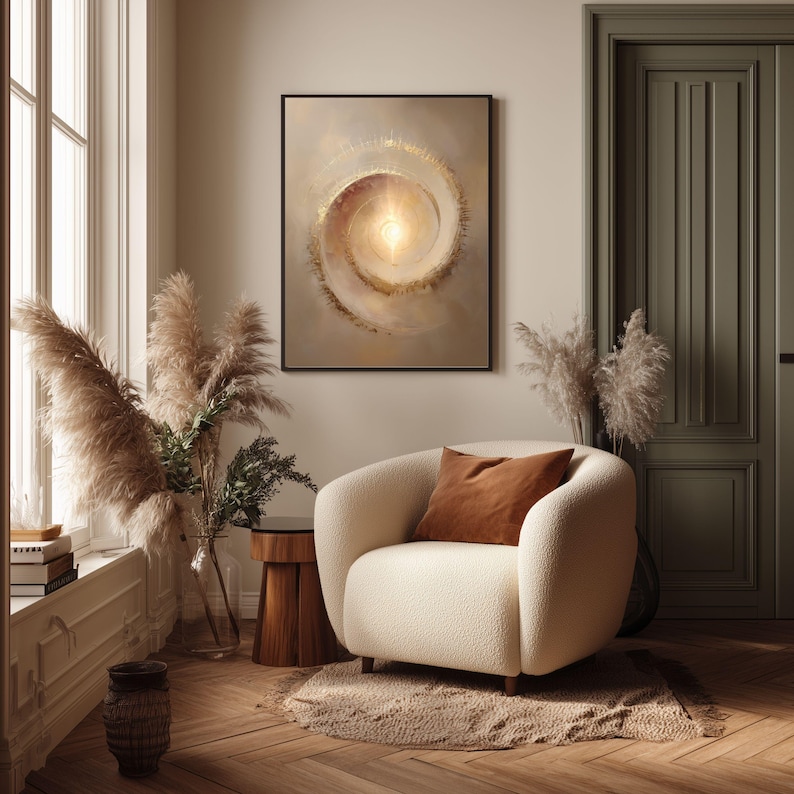 May include: A framed abstract art piece with a spiral design in beige and gold tones hangs above a cream-colored armchair. The room features a wooden floor, pampas grass, and a brown throw pillow.