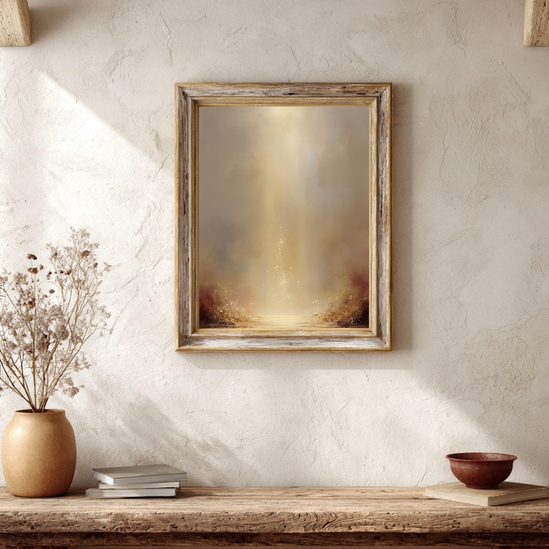 May include: A framed abstract art piece with a light brown wooden frame. The artwork features a warm, golden color palette with a central light source and a textured, blurred effect. The piece is displayed on a wooden surface.