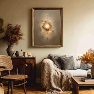 May include: A framed abstract art piece with a gold frame hangs on a wall. The artwork features a central bright light surrounded by soft, cloud-like shapes in shades of gold, beige, and brown. The room has a neutral color palette.