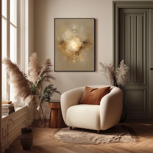 May include: An abstract art print in a black frame hangs above a cream-colored armchair with a brown pillow. The artwork features a central golden light surrounded by circular lines and a beige background. The room is decorated with pampas grass and a wooden side table.