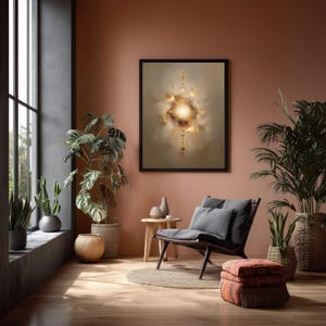 May include: A framed abstract art print with a central bright light and gold accents hangs above a dark wicker chair with gray cushions. The room features potted plants, a small wooden table, and a patterned ottoman. The walls are painted a warm terracotta color.