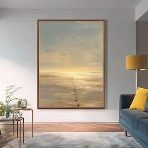 Può includere: Una stampa artistica da parete verticale incorniciata che raffigura un paesaggio di spiaggia sabbiosa al tramonto. La scena presenta una singola linea di impronte scure che si estende sulla sabbia dorata riflettente verso un orizzonte fosco.