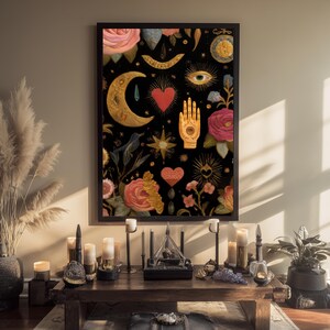 Peut inclure: Une affiche encadr&eacute;e avec un fond noir orn&eacute; d'&eacute;l&eacute;ments floraux dor&eacute;s et roses, d'un croissant de lune, d'une main avec un &oelig;il et de c&oelig;urs. L'affiche est expos&eacute;e au-dessus d'une table en bois avec des bougies et des objets d&eacute;coratifs.