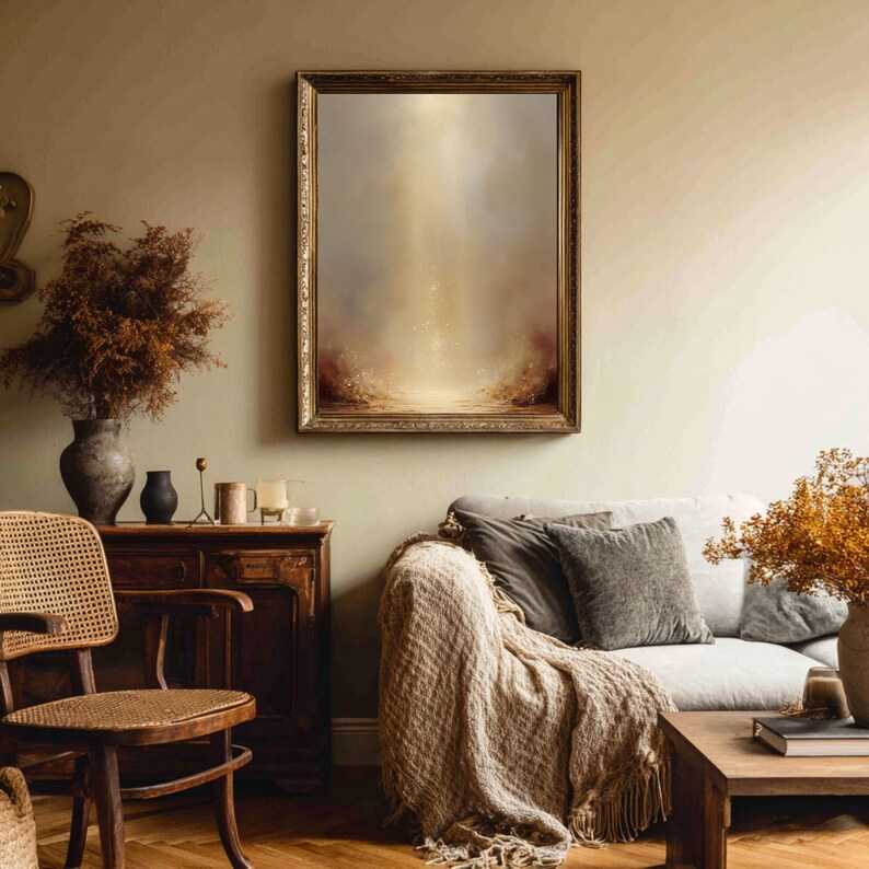 May include: An abstract painting in a gold ornate frame hangs above a sofa with a beige throw blanket. The painting features a light-filled, ethereal landscape with warm tones. A wooden chair and cabinet are in the foreground.