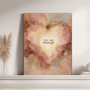 May include: A framed art print featuring a heart-shaped design with a soft, watercolor effect. The artwork uses a palette of pinks, browns, and gold accents, with the words "YOU ARE Enough" in the center. The frame is a warm brown.