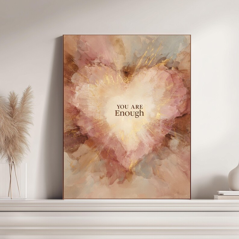 May include: A framed art print featuring a heart-shaped design with a soft, watercolor effect. The artwork uses a palette of pinks, browns, and gold accents, with the words "YOU ARE Enough" in the center. The frame is a warm brown.