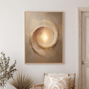 May include: Abstract art print featuring a spiral design with a bright, golden center. The artwork is framed in a light wood frame and hangs on a neutral-toned wall. The spiral artwork has a warm color palette with gold and beige tones.