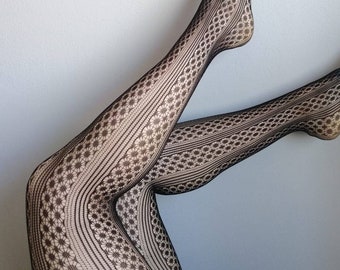 May include: Black patterned tights with a floral and geometric design. The tights are made of a sheer material and cover the legs and feet. The pattern is visible against the skin.
