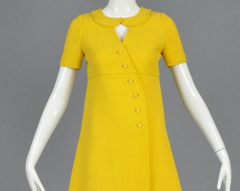 May include: A yellow mini dress with a Peter Pan collar and a row of buttons down the front. The dress has short sleeves and a slightly A-line silhouette.