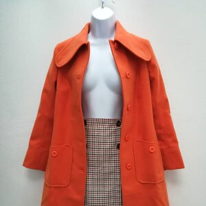 May include: A bright orange coat with a large collar and two pockets. The coat is on a white mannequin and has a button closure.
