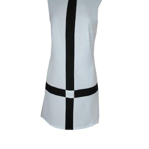 May include: A sleeveless white dress with a black vertical stripe down the center and a black horizontal stripe across the bottom. The dress has a mock neck.
