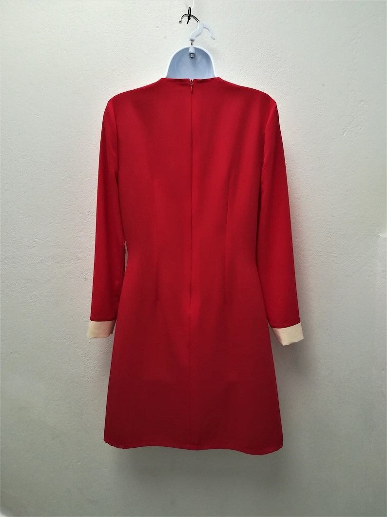 May include: A red dress with long sleeves and a white trim on the cuffs. The dress has a round neckline and a zipper in the back.