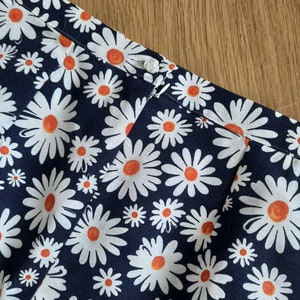 May include: A navy blue fabric with a white daisy pattern. The daisies have orange centers.