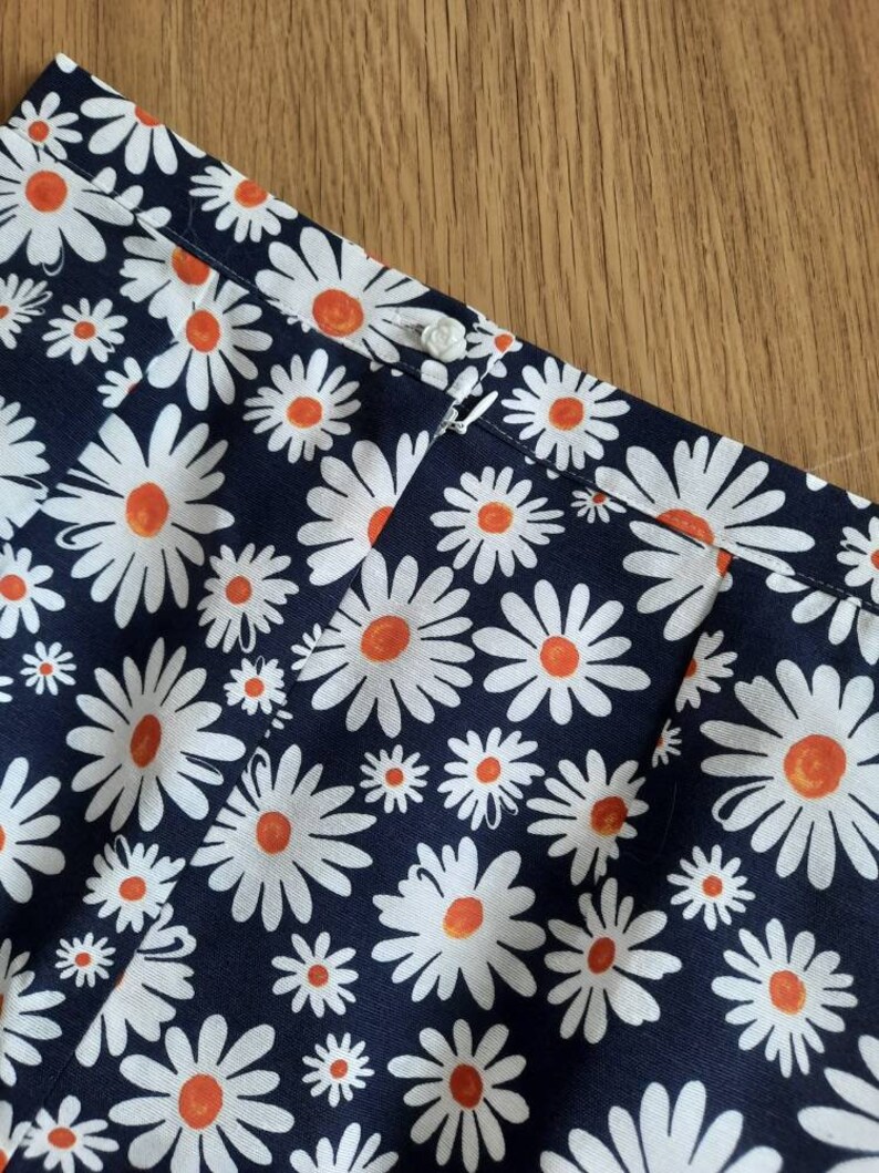 May include: A navy blue fabric with a white daisy pattern. The daisies have orange centers.