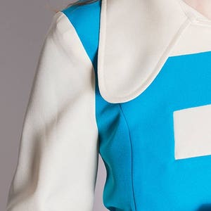 May include: A close-up of a blue and white jacket with a large white collar. The jacket has a geometric design with a white square on the blue section.