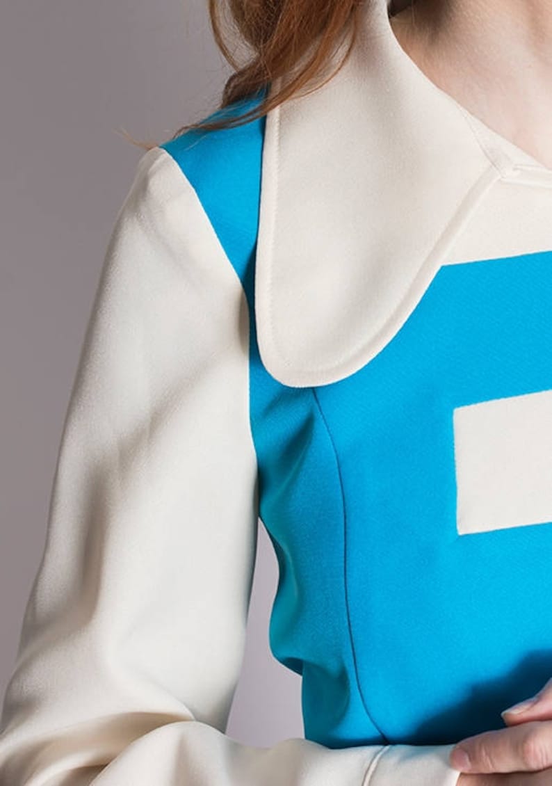 May include: A close-up of a blue and white jacket with a large white collar. The jacket has a geometric design with a white square on the blue section.