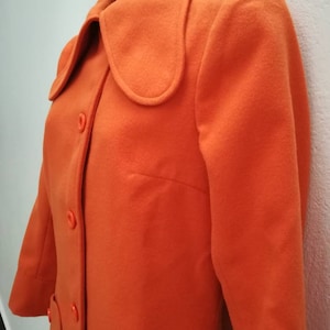 May include: A long-sleeved orange coat with a large collar and button closure. The coat has two large pockets on the front.