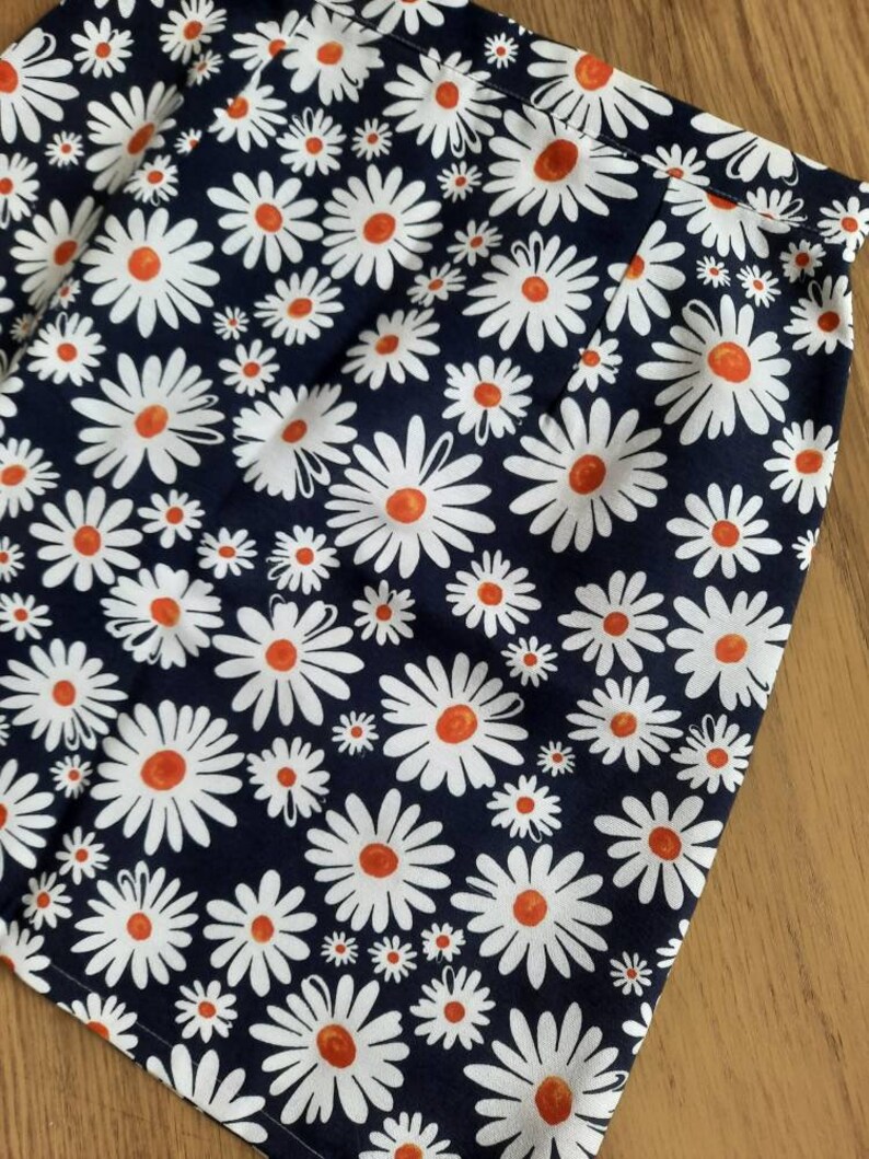 May include: A navy blue skirt with a white daisy print. The daisies have orange centers.