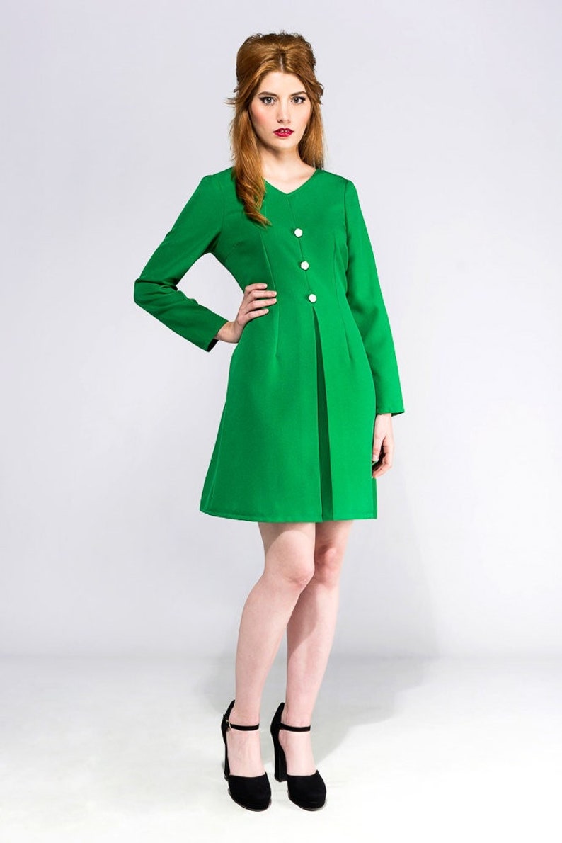 May include: A woman wearing a green dress with white buttons and black heels. The dress has a v-neck and long sleeves.