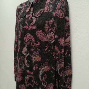 May include: A long-sleeved dress with a paisley print in shades of pink, brown, and white on a black background. The dress has a collared neckline and button closure.