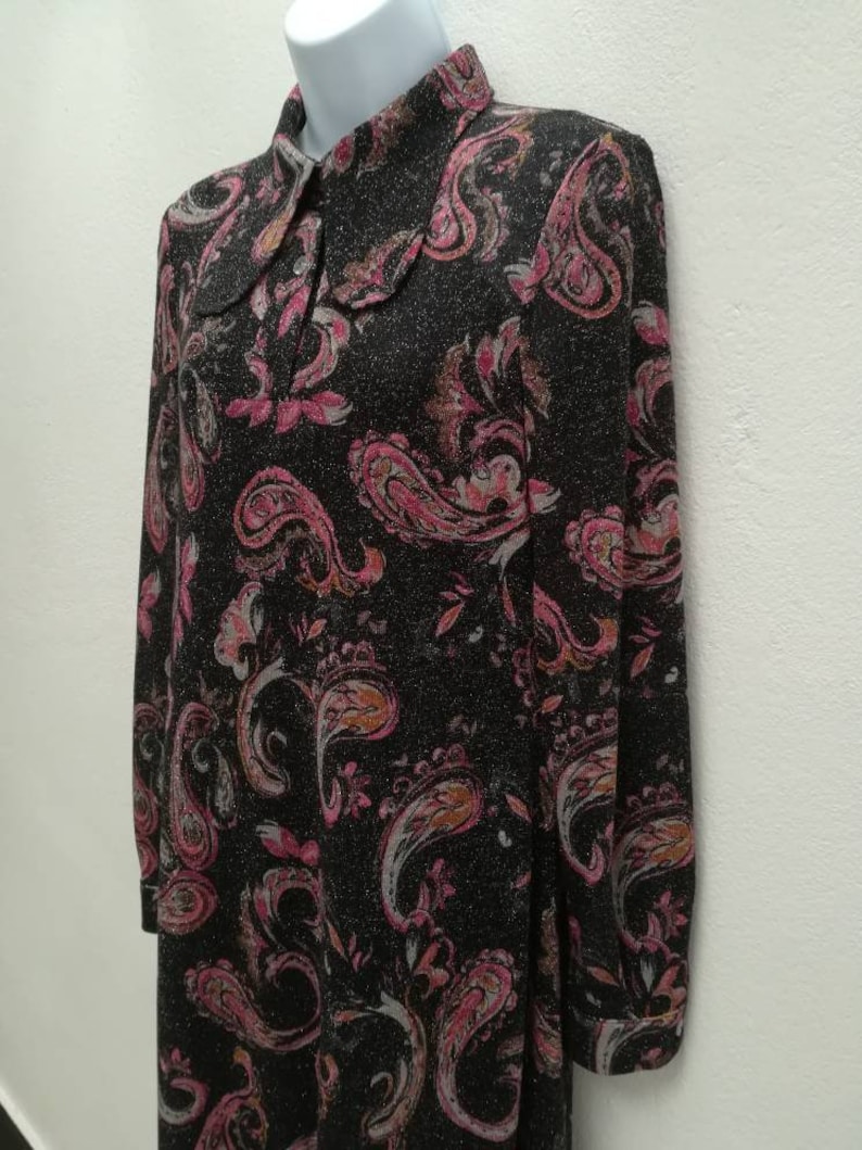 May include: A long-sleeved dress with a paisley print in shades of pink, brown, and white on a black background. The dress has a collared neckline and button closure.