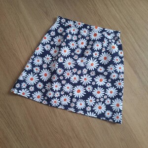 May include: A navy blue skirt with a white daisy print. The daisies have orange centers.