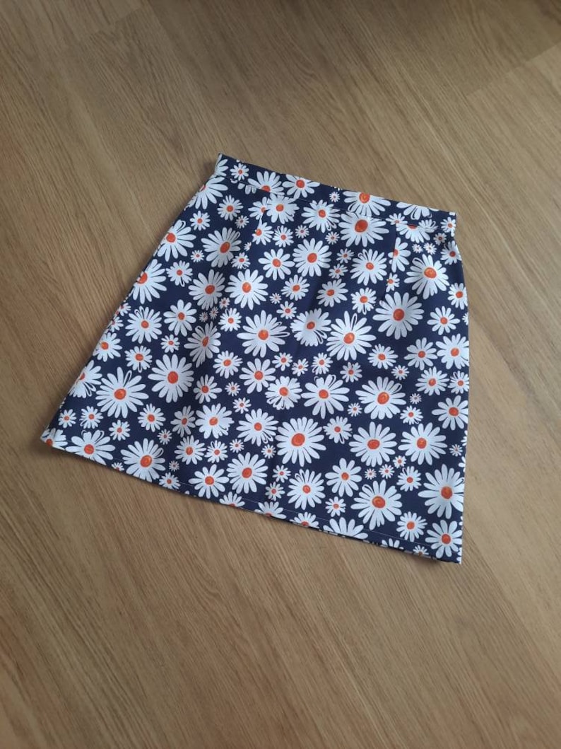 May include: A navy blue skirt with a white daisy print. The daisies have orange centers.